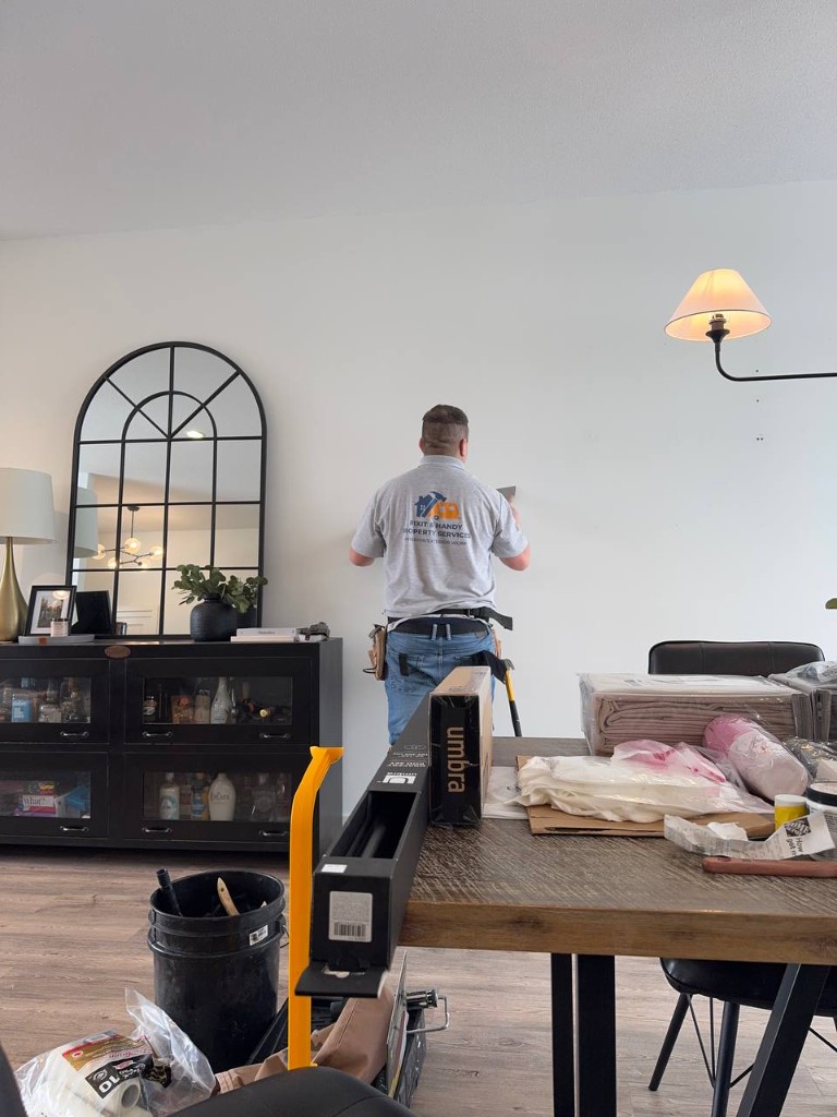Fixit & Handy technician working on an interior door with floor protection and painter's tape.