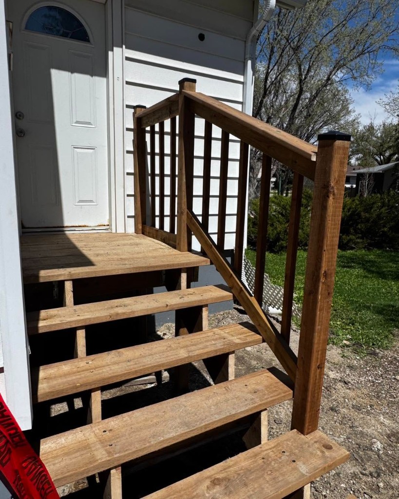 Newly built wooden exterior stairs with handrail leading to a residential front door.