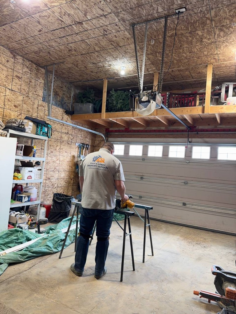 Painter rolling a dark accent wall with furniture protected by drop cloths.