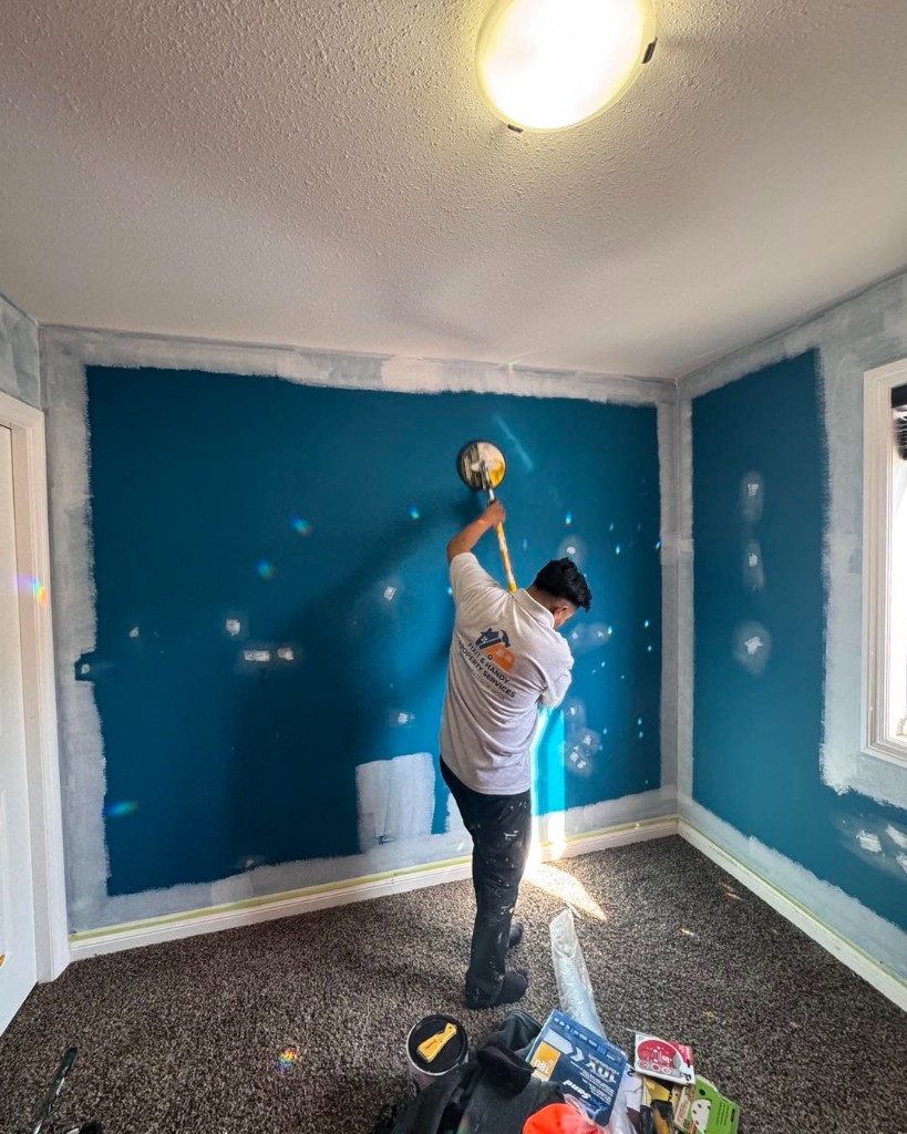 Technician in Fixit & Handy branded shirt sanding a painted interior wall during prep work.