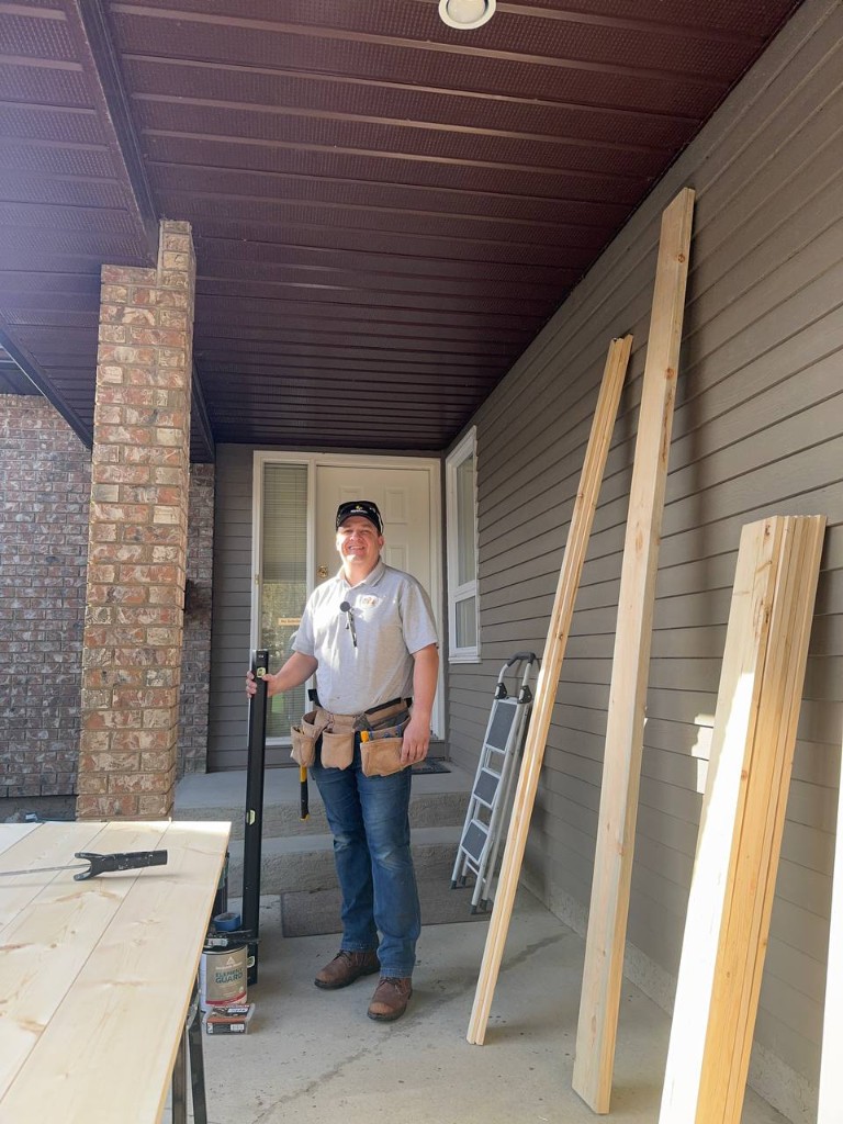 Fixit & Handy craftsman on a home porch with tool belt and level, ready for professional handyman work.